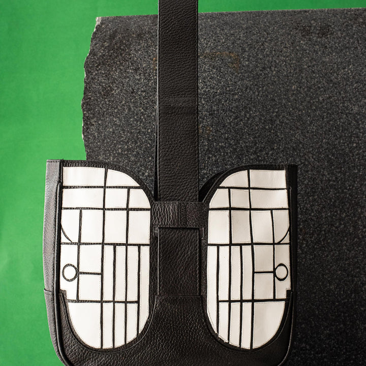 Black and white leather handbag with grid pattern, displayed on textured stone surfaces with green background