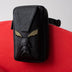 Black leather crossbody bag with embossed face design and gold accents on red chair