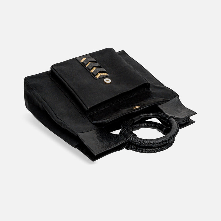 Black canvas tote bag with round woven leather handles and front pocket featuring gold chevron details