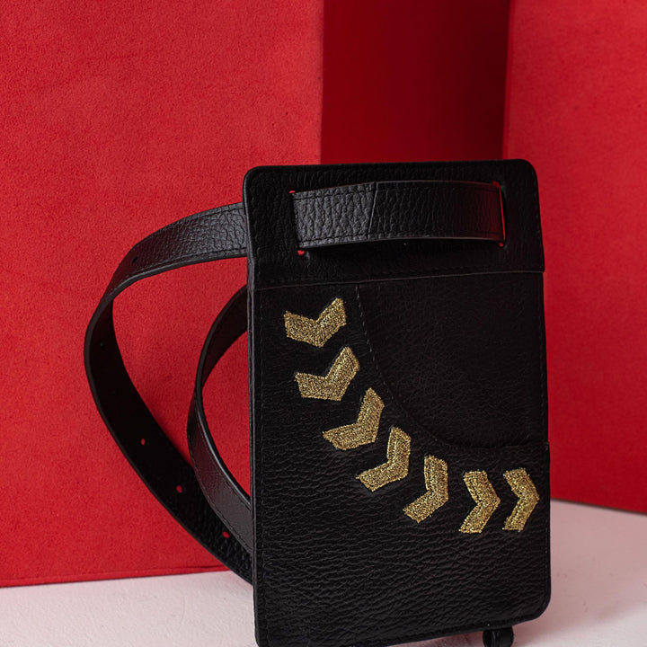 Black leather belt bag with gold chevron pattern, standing against red geometric background