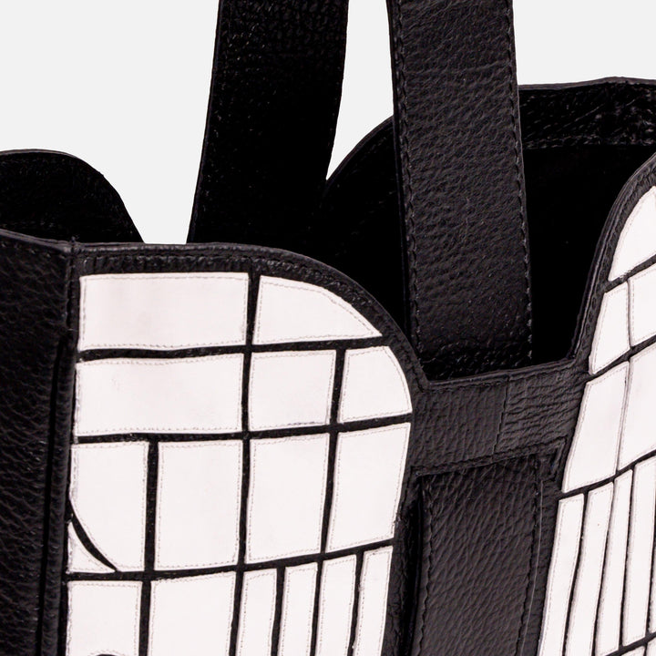 Close-up of black leather bag with white grid pattern and wide straps
