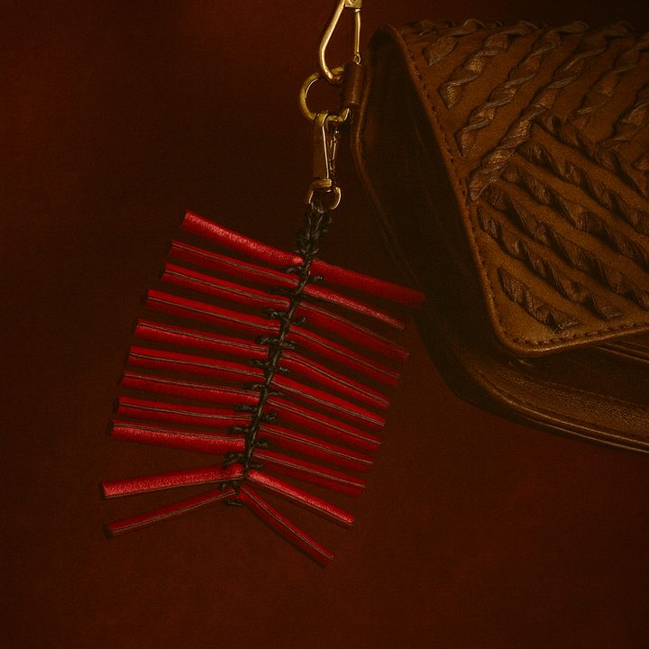 Brown woven leather handbag with red leather tassel keychain on a dark brown background