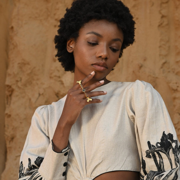 Woman with natural afro hairstyle wearing beige dress with black floral embroidery and gold finger ring