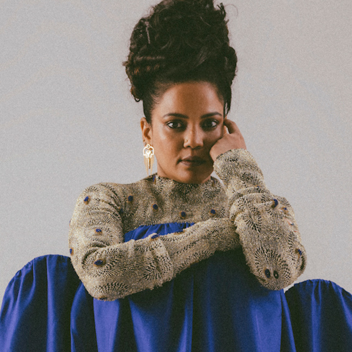 Portrait of a woman with curly updo wearing a textured beige top with blue accents and a flowing blue skirt