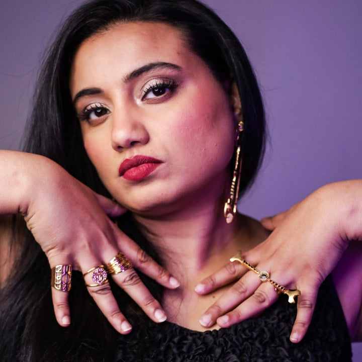 Close-up portrait of woman with red lipstick and gold rings posing against purple background