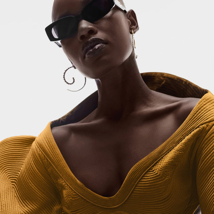 Fashion model wearing mustard yellow textured top, black sunglasses, and large gold hoop earrings