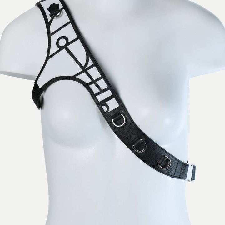 Black leather one-shoulder harness with metal D-rings and geometric applique on mannequin bust
