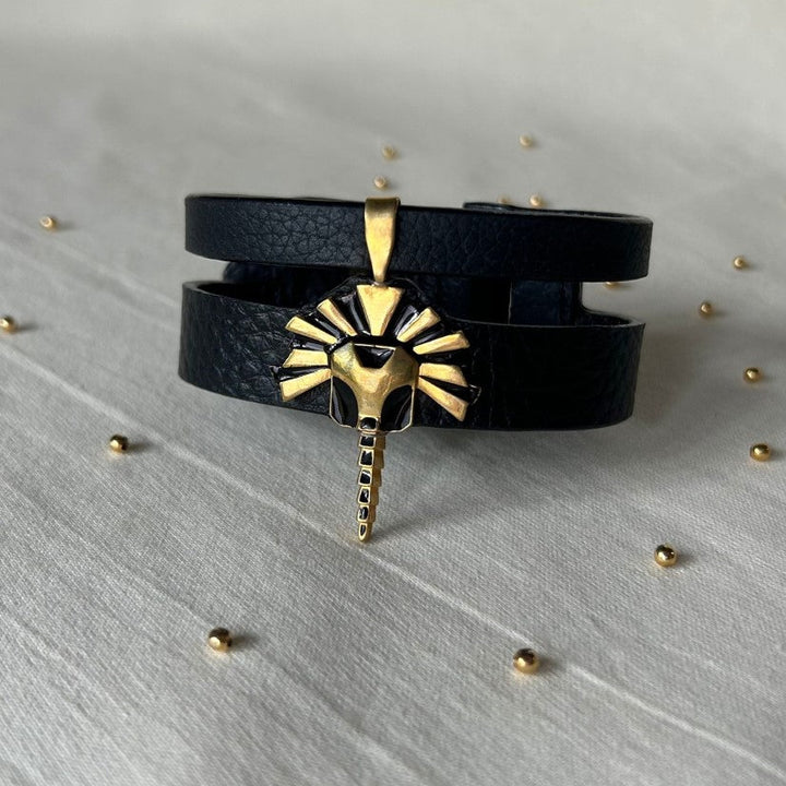 Timeless black leather wrap bracelet with gold lion head pendant on light fabric surface with small gold beads