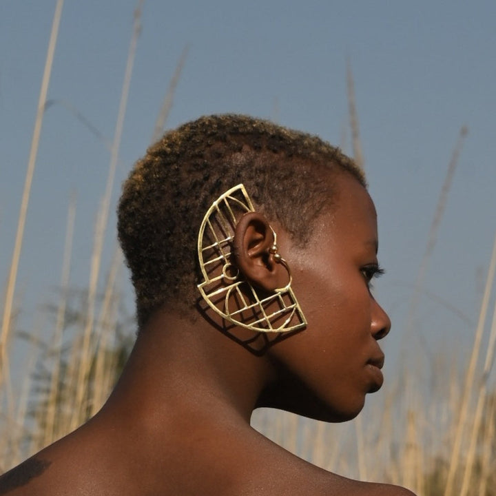 Profile of woman with short hair wearing large geometric gold statement earring outdoors