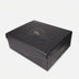 Black textured rectangular gift box with embossed gold logo on lid, white background