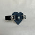 Black leather cuff bracelet with heart-shaped centerpiece and silver ring studs on neutral background