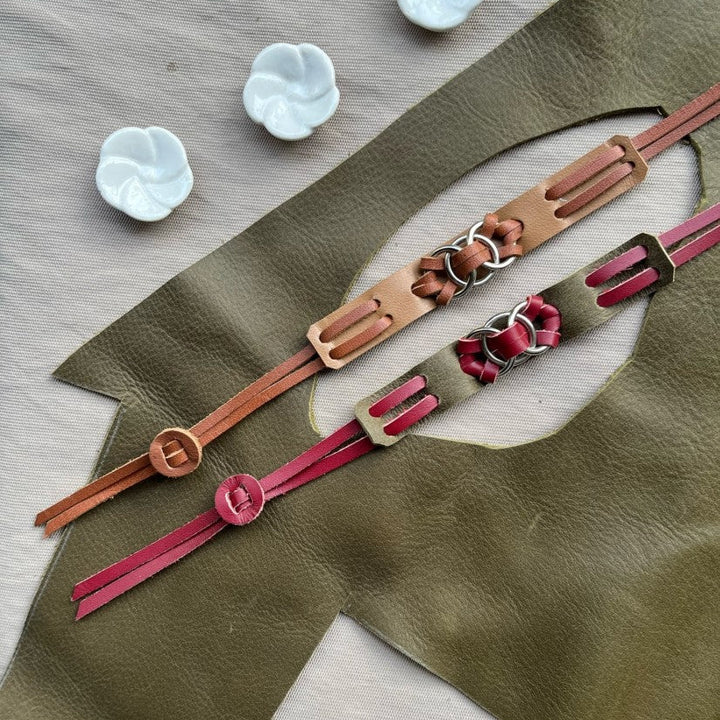 Handcrafted leather bracelets with intricate metal ring details on olive green leather backdrop and white ceramic flower beads