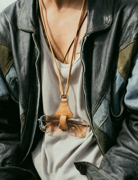 Close-up of person wearing a vintage leather jacket and eyeglasses hanging on a leather strap around the neck