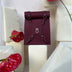 Maroon leather roll-top backpack with silver buckles, displayed on white foam blocks with red anthurium flowers