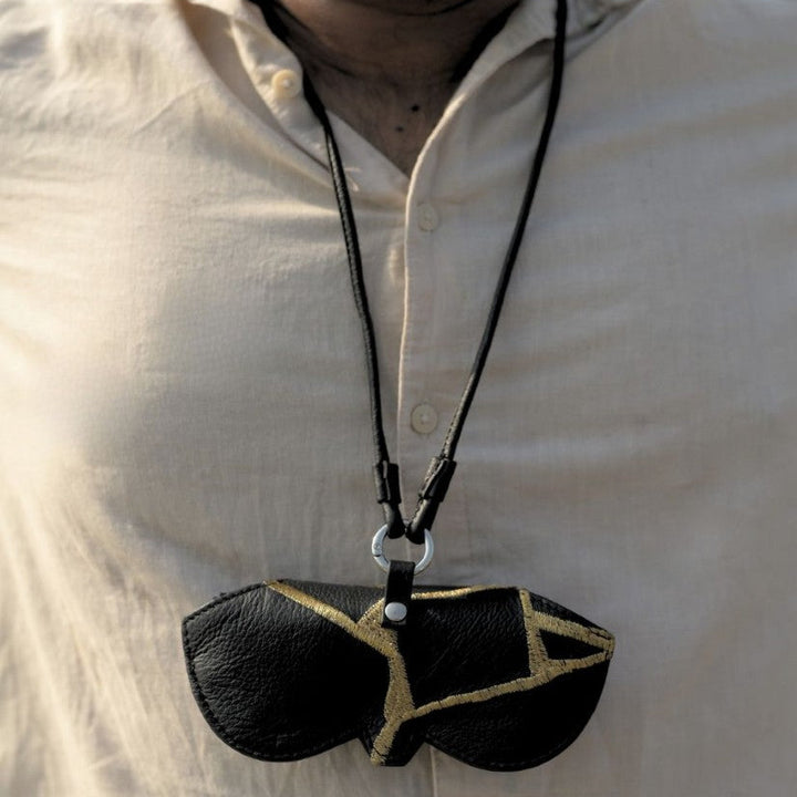 Man wearing beige shirt with black leather sunglasses pouch necklace featuring gold geometric design