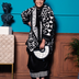 Smiling woman in black and white geometric print outfit holding matching handbag, standing by blue wall