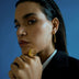 Close-up of woman wearing geometric gold statement ring and matching earrings against blue background