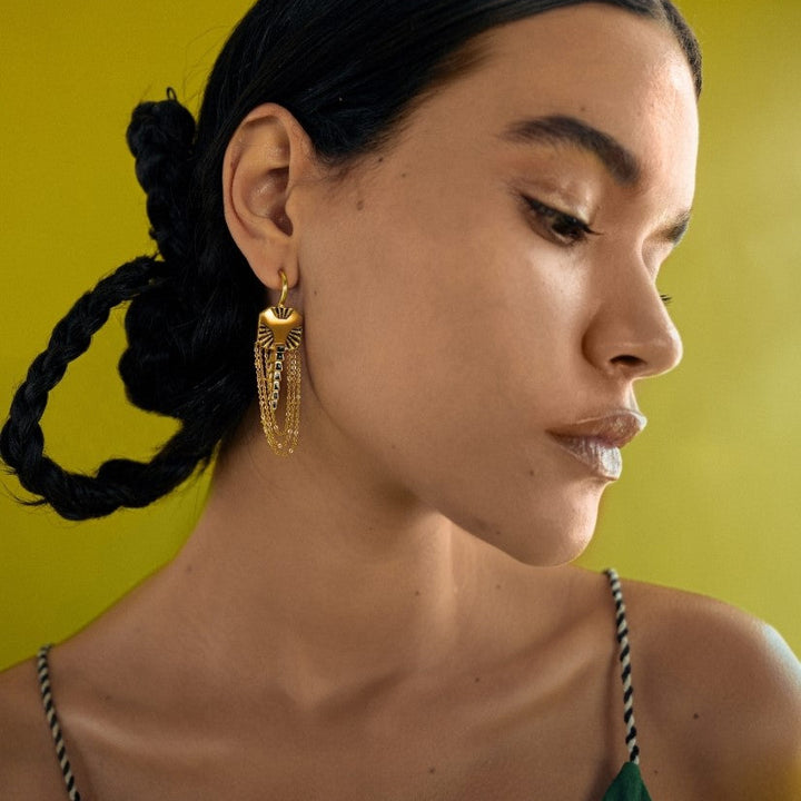 Close-up of woman with braided hair wearing gold chain earrings against yellow background