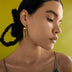 Close-up of woman with braided hair wearing gold chain earrings against yellow background