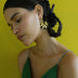 Woman wearing green dress and black enamel gold earrings with spiral design against yellow background