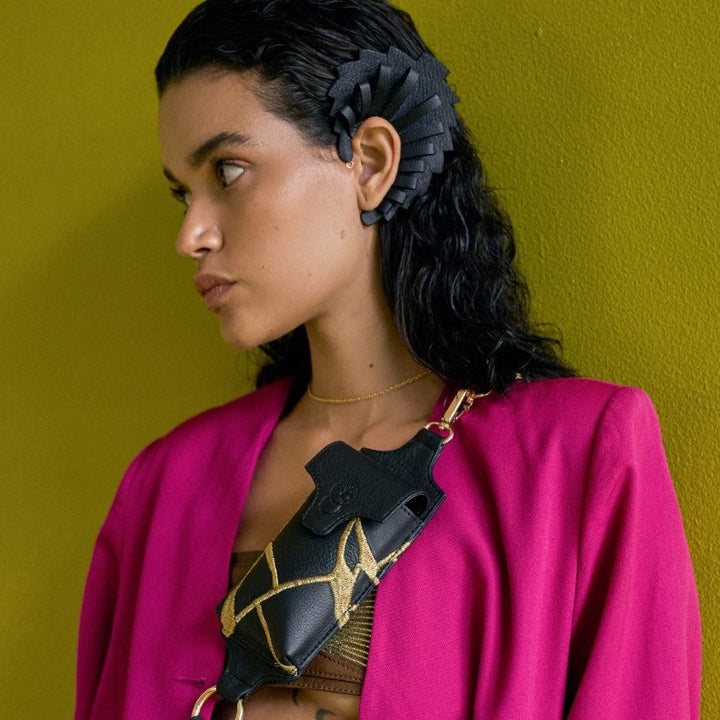 Woman wearing black leather upcycled ear cuff and black leather bag with gold embroidery, fuchsia blazer, green background