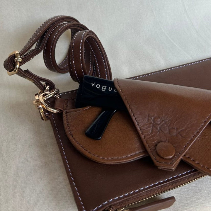 Timeless tan leather crossbody bag with white stitching and a black Vogue sunglass partially tucked in the front pocket