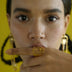 Close-up of woman with dark hair wearing gold geometric statement ring and matching earrings against yellow background