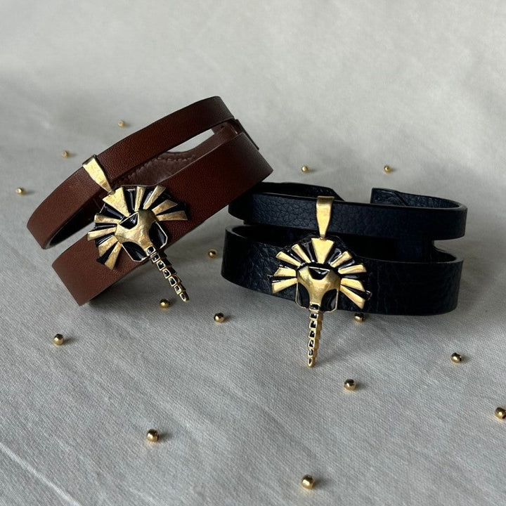 Handcrafted upcycled leather bracelets in brown and black with gold lion head charms displayed on fabric surface with small gold beads