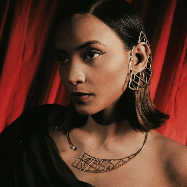 Portrait of woman wearing geometric metal ear cuff and matching necklace against red curtain backdrop