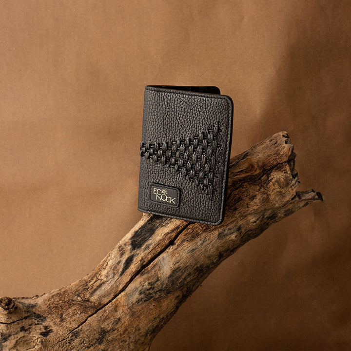 Black textured leather wallet with stitched triangular pattern and logo on natural wooden branch