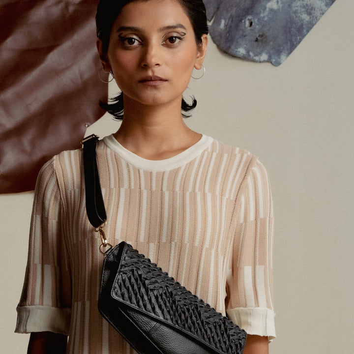 Woman wearing beige patterned dress and black textured leather crossbody bag with gold clasp