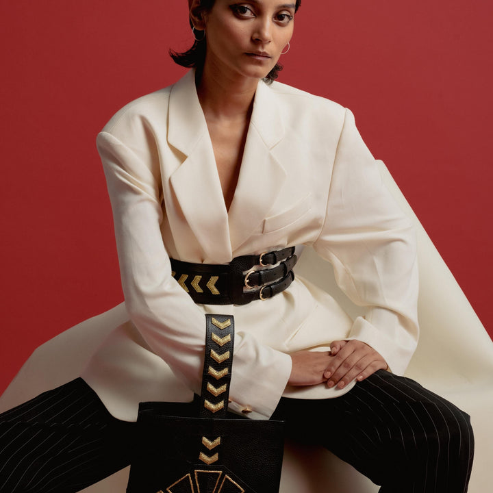 Stylish woman in oversized white blazer with black belt and pinstripe pants holding black bag with gold design