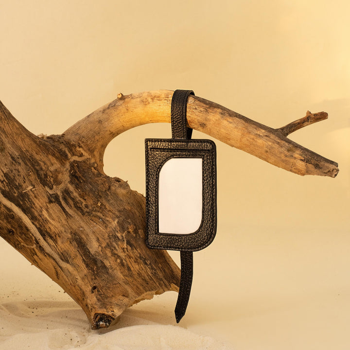 Black leather luggage tag hanging on rustic driftwood with sandy beige background