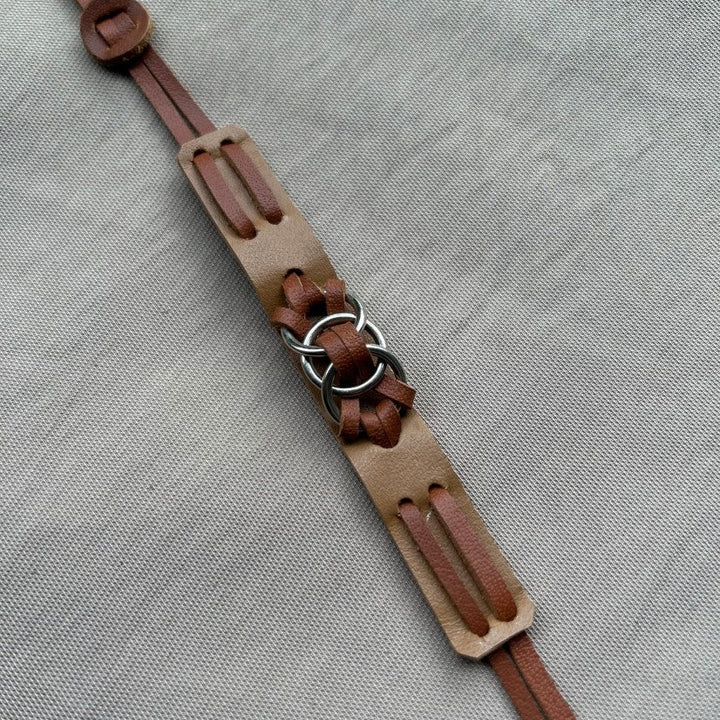 Brown leather strap with metal rings laid on textured gray fabric