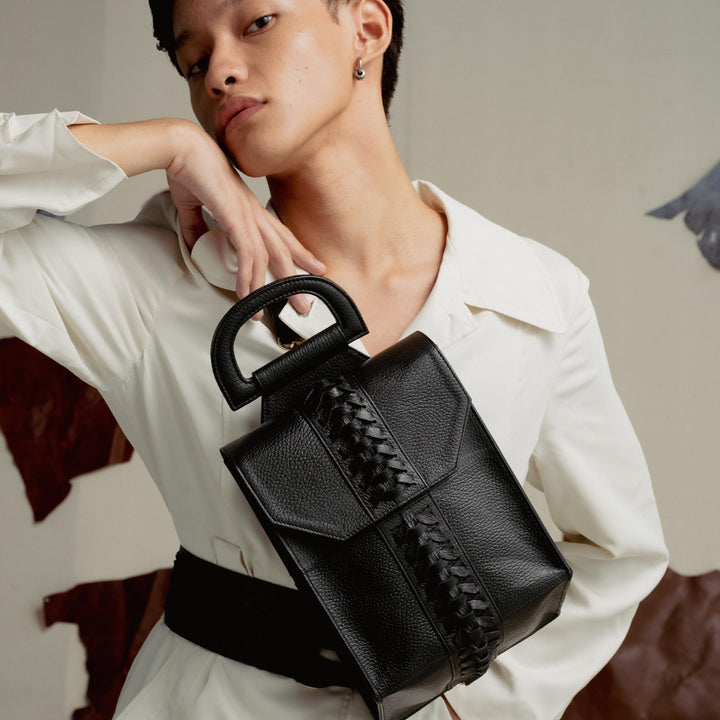 Stylish person in white outfit posing with a black leather handbag with braided detail