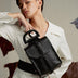 Stylish person in white outfit posing with a black leather handbag with braided detail