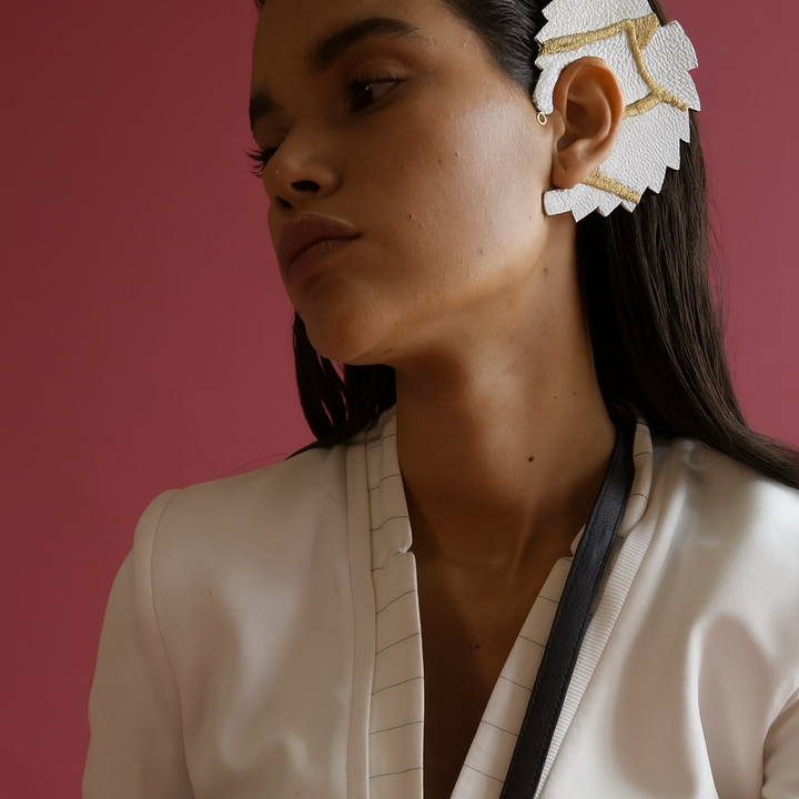 Woman with sleek dark hair wearing white leather and gold embroidered leaf-shaped adjustable ear cuff against pink background