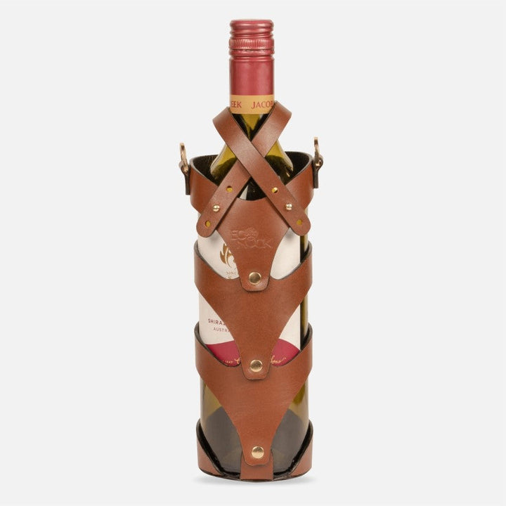 Wine bottle secured in tan stitched upcycled leather case with brass studs on white background