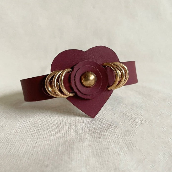 Timeless burgundy leather cuff bracelet with gold ring studs and heart centerpiece on light fabric