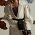 Fashionable woman in white suit with puffy sleeves, embroidered collar, black belt bag and clutch