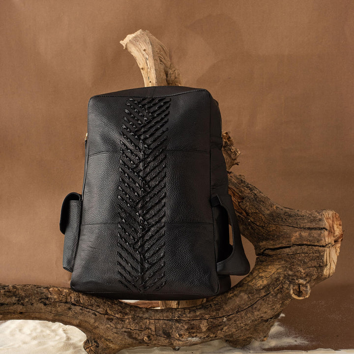 Designer Black leather backpack with braided detailing displayed on a rustic wooden branch against brown background