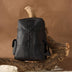 Designer Black leather backpack with braided detailing displayed on a rustic wooden branch against brown background