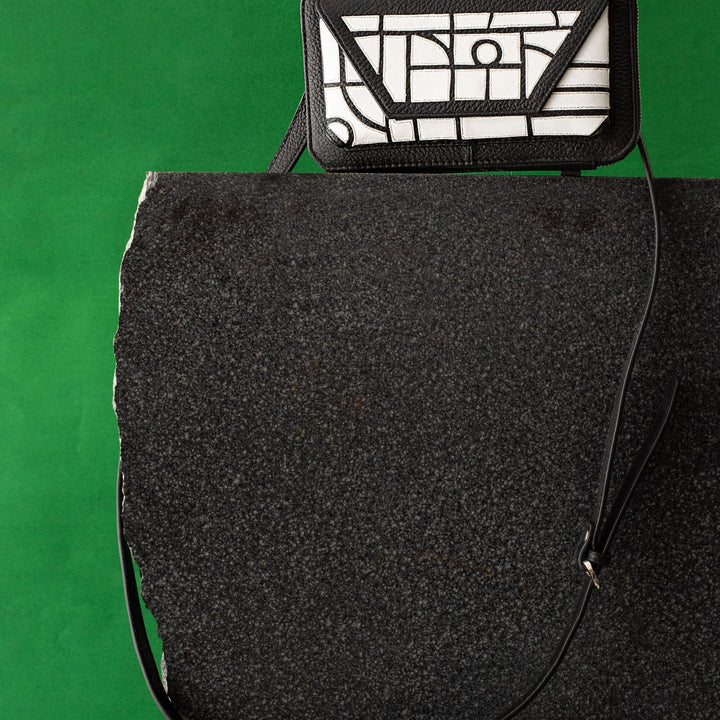 Black and white geometric-patterned leather crossbody bag on black stone with green background