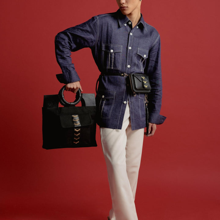 Young man in dark denim shirt with stitched details, white pants, carrying black handbags on red background