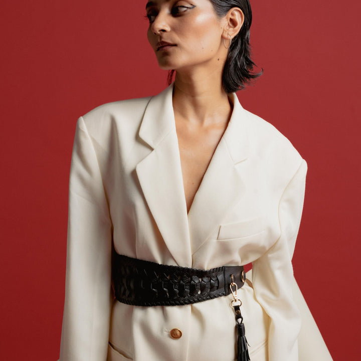 Woman in white oversized blazer with gold buttons and black woven belt against red background