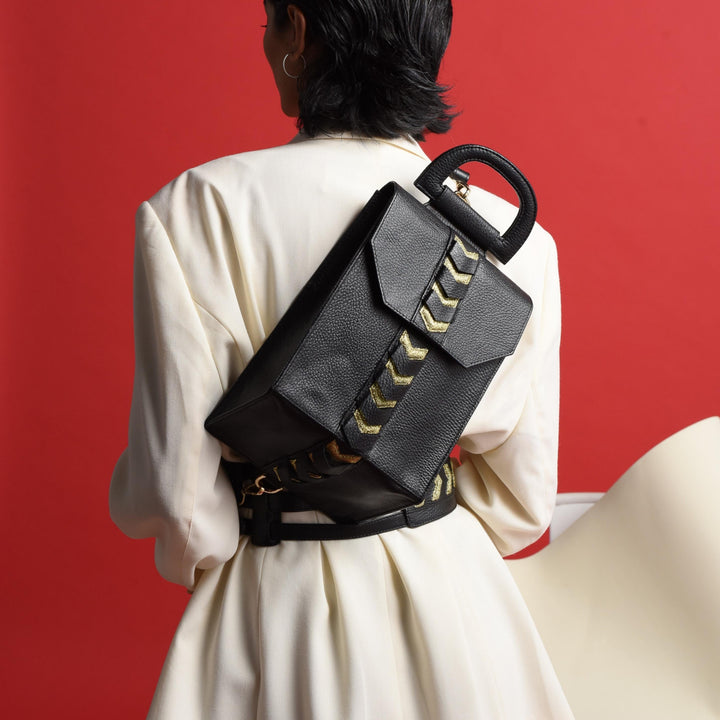 Back view of woman in white blazer wearing black leather backpack with gold arrow detail against red background