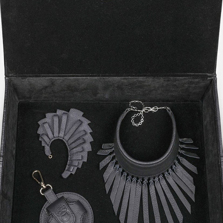 Elegant black leather jewelry set with fringe necklace, matching earrings, and round keychain in a black velvet box
