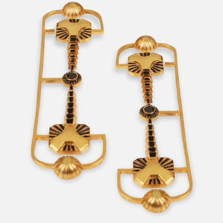Handcrafted gold-tone metal earrings with embossed black enamel details on white background