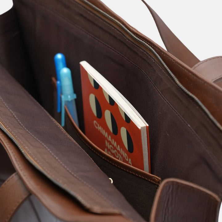 Brown leather tote bag interior with pens and a small book featuring a red and black patterned cover