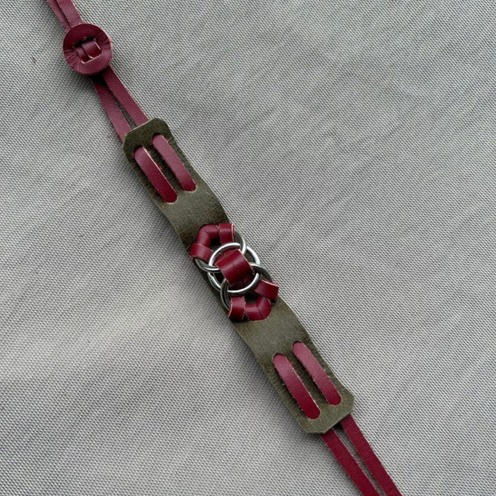 Handmade leather bracelet with burgundy straps and metal rings on gray fabric background